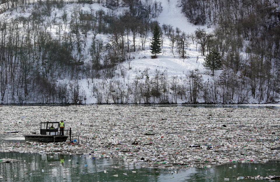 A boat pushes tons of garbage stuck at the foot of the hydro power plant at the Potpecko accumulation lake near Priboj, in southwest Serbia, Friday, Jan. 22, 2021. Serbia and other Balkan nations are virtually drowning in communal waste after decades of neglect and lack of efficient waste-management policies in the countries aspiring to join the European Union. (AP Photo/Darko Vojinovic)