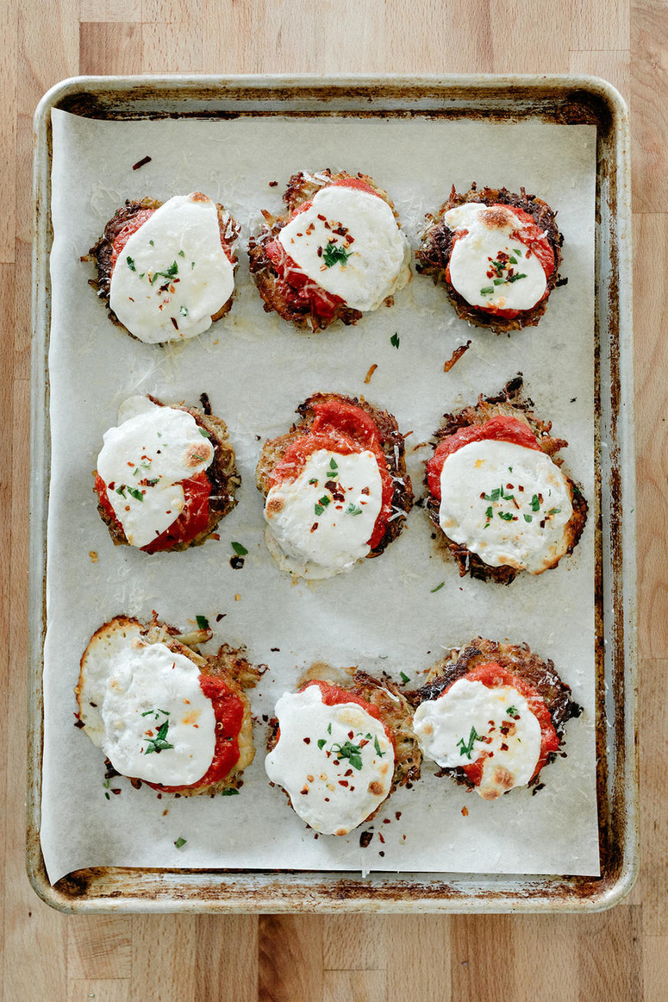 A baking sheet lined with latkes topped with tomato sauce and mozzarella cheese.