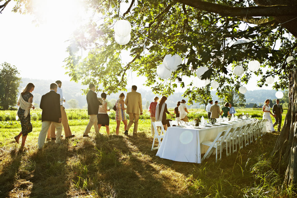 Bride and groom and wedding party walking to banquet table set for dinner outside under tree in field