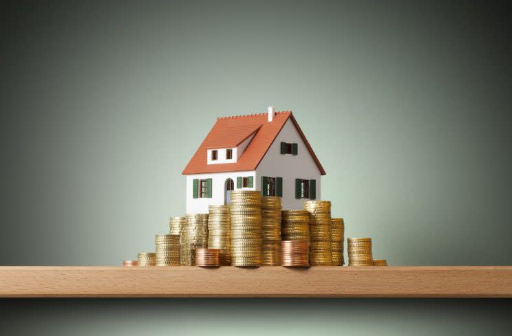 Miniature model house standing on a stack of coins.