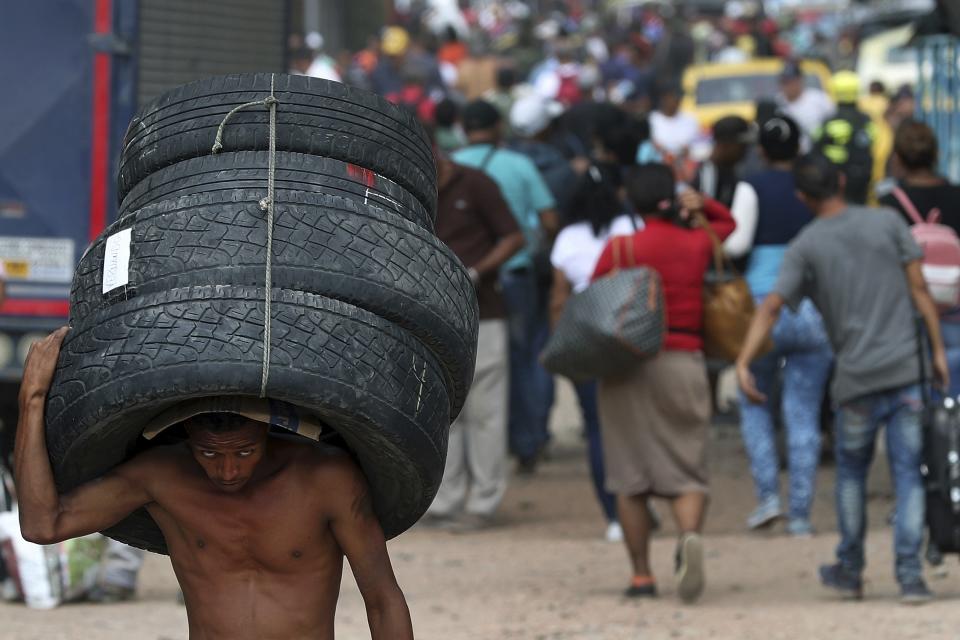 A man carries a set of used tires into Venezuela, through a blind spot on the border near the Simon Bolivar International Bridge in La Parada, Colombia, Thursday, Feb. 28, 2019. The tires were bought in Cucuta, Colombia and carried across the border into Venezuela. (AP Photo/Martin Mejia)