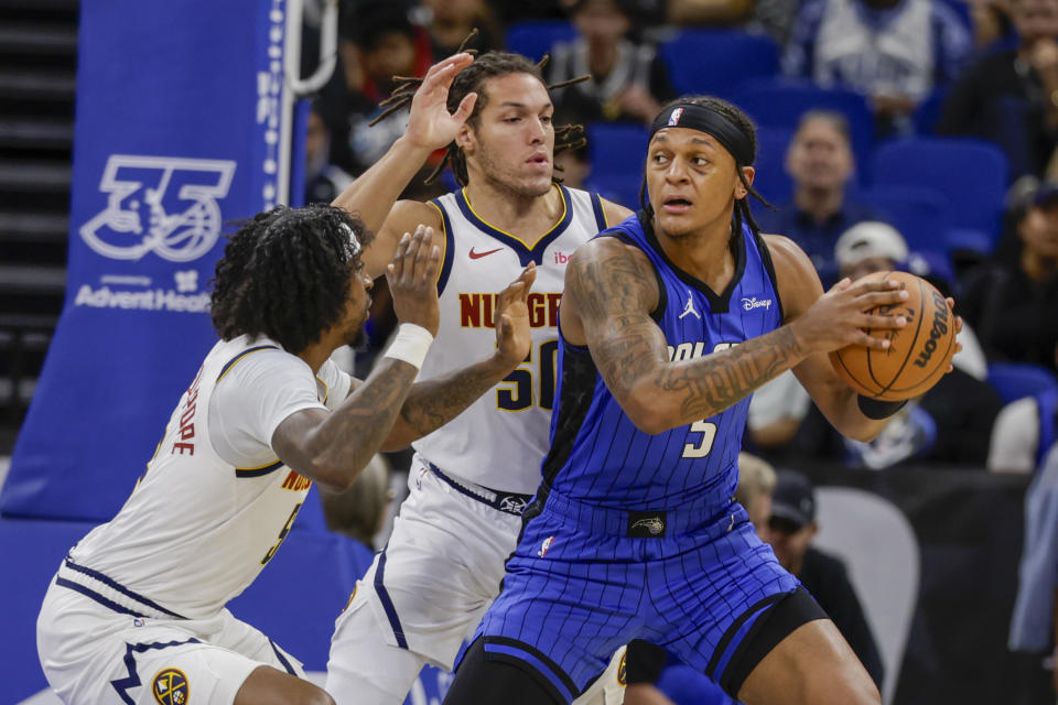 Orlando Magic forward Paolo Banchero, right, is defended by Denver Nuggets guard Kentavious Caldwell-Pope, left, and forward Aaron Gordon, middle, during the first half of an NBA basketball game Wednesday, Nov. 22, 2023, in Orlando, Fla. (AP Photo/Kevin Kolczynski)