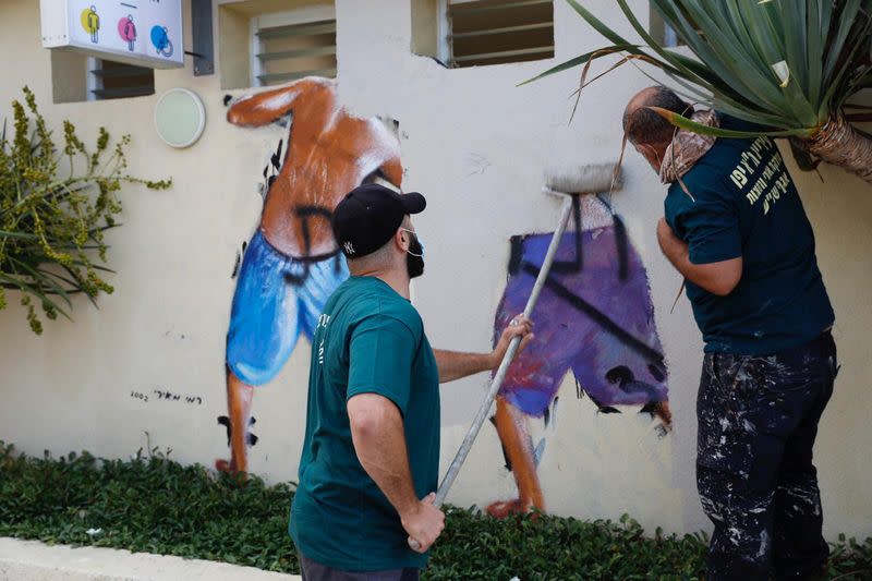 Workers clean the "Peeping Toms" mural at the beach in Tel Aviv