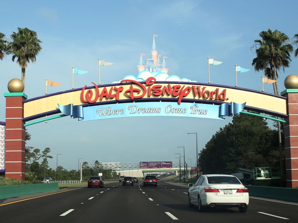 Cars driving on a road under a sign for Walt Disney World in Orlando, Florida.