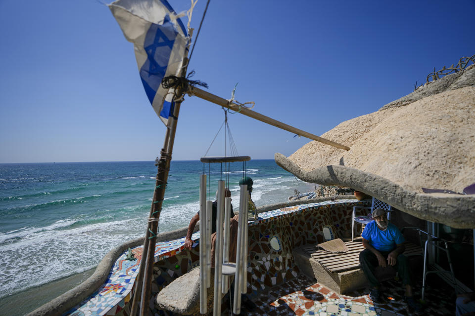 Nissim Kahlon sits in his balcony in his home chiseled out of the sandstone cliffs overlooking the Mediterranean sea in Herzliya, Israel, Wednesday, June 28, 2023. Over half a century, Kahlon has transformed a tiny cave on a Mediterranean beach into an elaborate underground labyrinth filled with chiseled tunnels, detailed mosaic floors and a network of staircases and mysterious chambers. Fifty years after Kahlon moved into the home, Israel's Environmental Protection Agency has served him an eviction notice, claiming the structure threatens Israel's coastline. (AP Photo/Ariel Schalit)