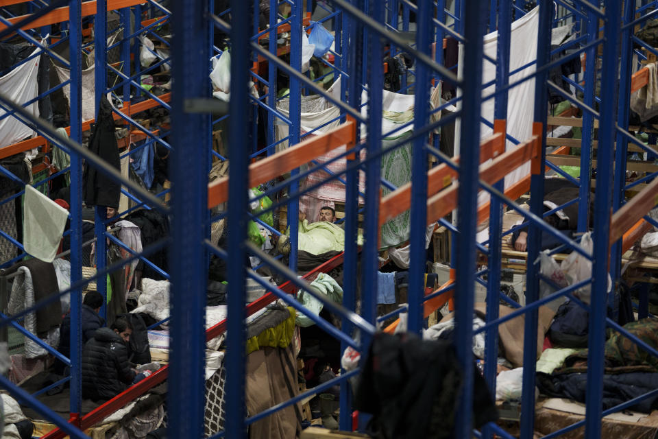 A man prepares to sleep as migrants settle at the "Bruzgi" checkpoint logistics center at the Belarus-Poland border near Grodno, Belarus, Thursday, Dec. 23, 2021. Since Nov. 8, a large group of migrants, mostly Iraqi Kurds, has been stranded at a border crossing with Poland. Most of them are fleeing conflict or hopelessness at home, and aim to reach Western European countries. But as temperatures fall below freezing, life at the border becomes more challenging. (AP Photo/Pavel Golovkin)