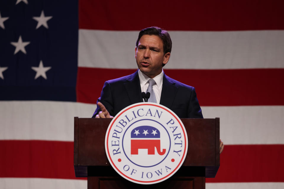 Ron DeSantis stands in front of American flag at a podium emblazoned with plaque reading: Republican Party of Iowa