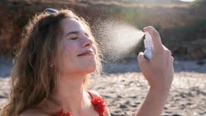 Young woman applying suncream spray on the beach