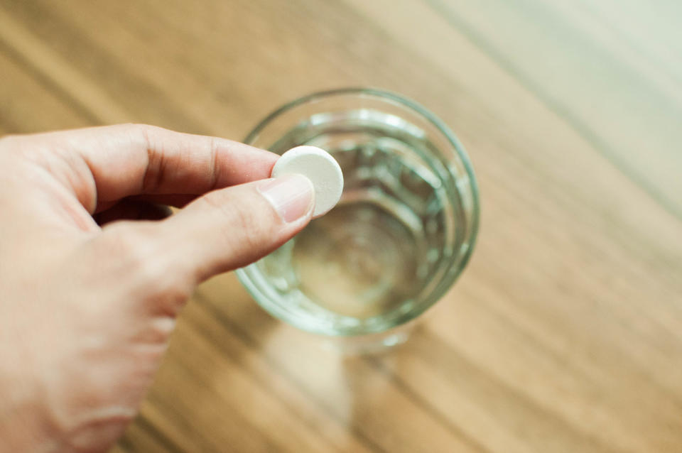 Hand holding a tablet over a glass of water. 