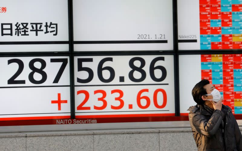 FILE PHOTO: A man wearing a protective mask, amid the coronavirus disease (COVID-19) outbreak, stands in front of an electric board showing Nikkei index outside a brokerage in Tokyo