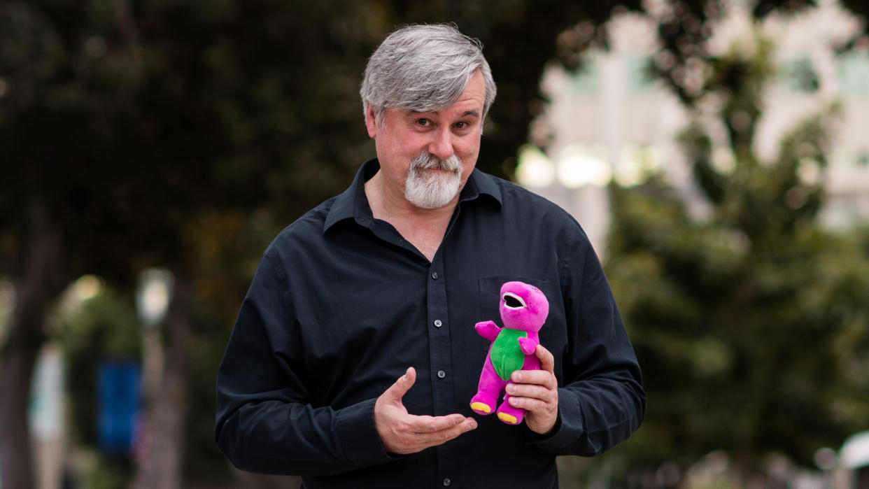 Bob West holding a Barney plush doll. (Peacock)