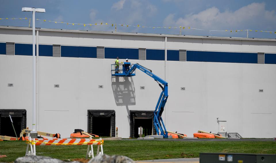 A blue cherry pocker with workers on it against a large white warehouse wall.