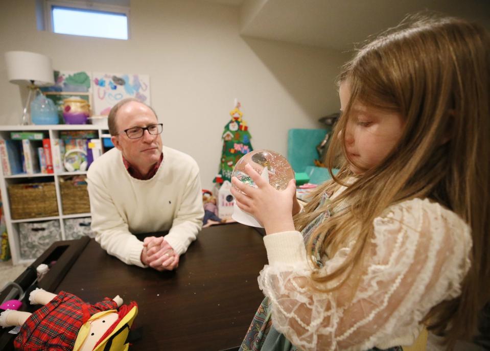 Rich Wilson watches as LJ Horvath, 5, holds a snow globe in the playroom at her family's Lafayette Township home.