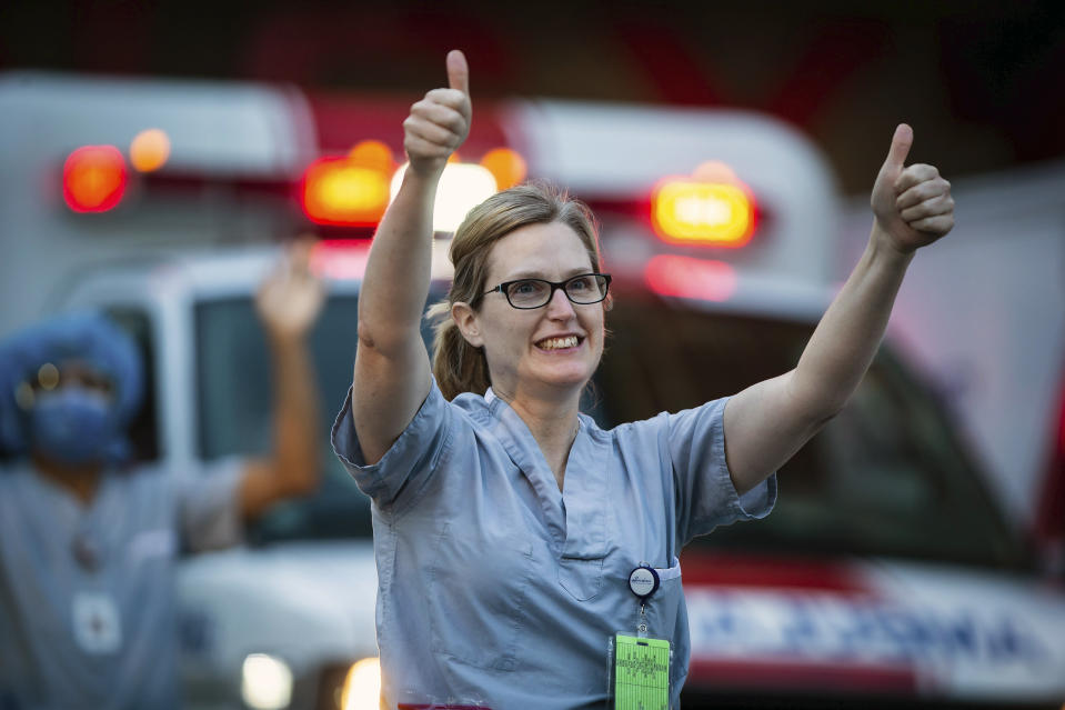 A healthcare worker at St. Paul's Hospital acknowledges applause and cheers from people outside the hospital, as a convoy of first responders with lights and sirens activated parade past to show support for the hospital staff, in Vancouver, British Columbia, Sunday, April 5, 2020. (Darryl Dyck/The Canadian Press via AP)