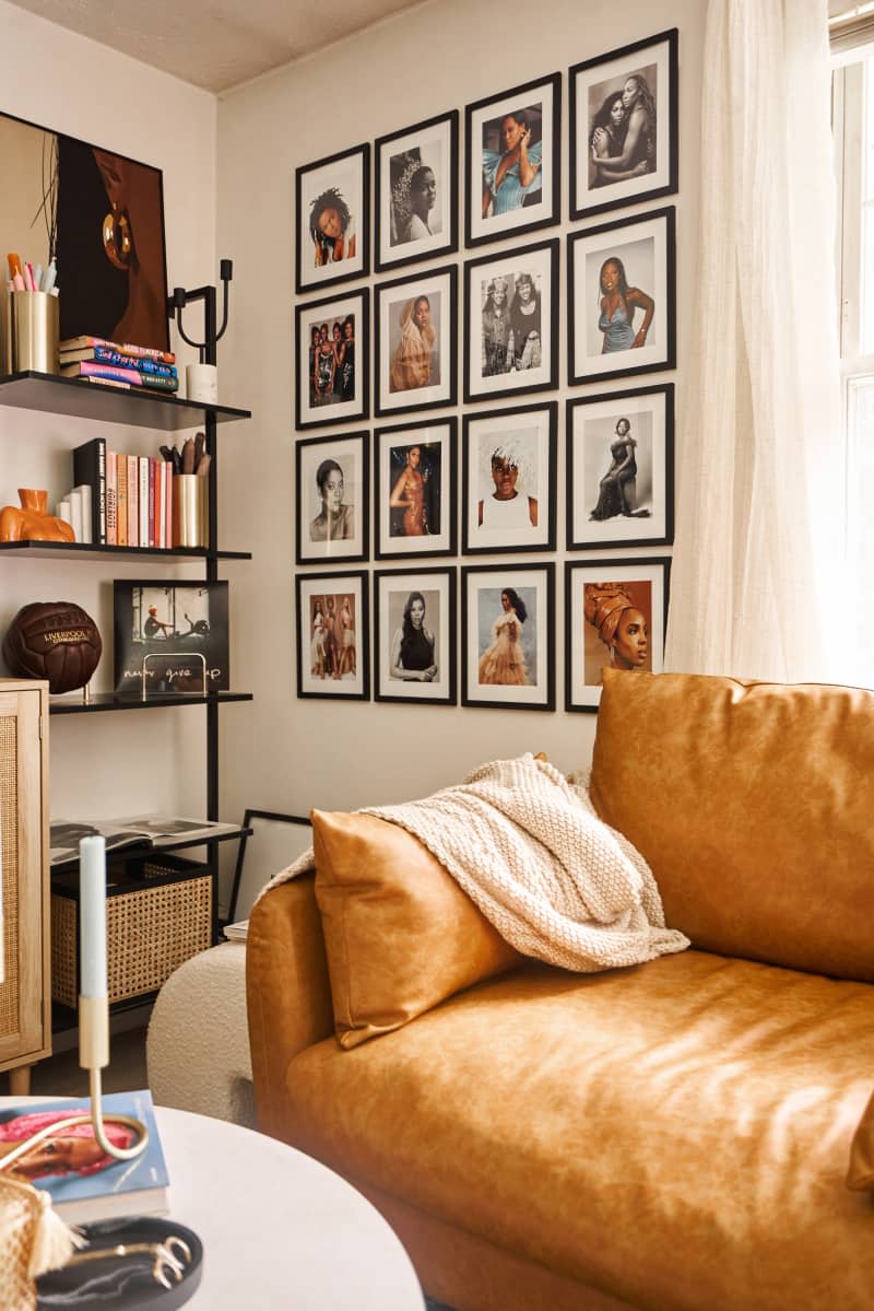 corner of white living room with camel leather armchair, grid style gallery wall, and black tall shelves