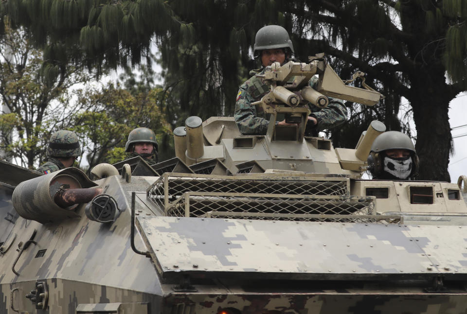 Soldiers in a fast-moving convoy ride in an armored vehicle during a 24-hour military curfew after violent protests across Quito, Ecuador, Sunday, Oct. 13, 2019. The government and indigenous protesters planned to begin negotiations aimed at defusing more than a week of demonstrations against a plan to remove fuel subsidies as part of an International Monetary Fund austerity package. (AP Photo/Dolores Ochoa)