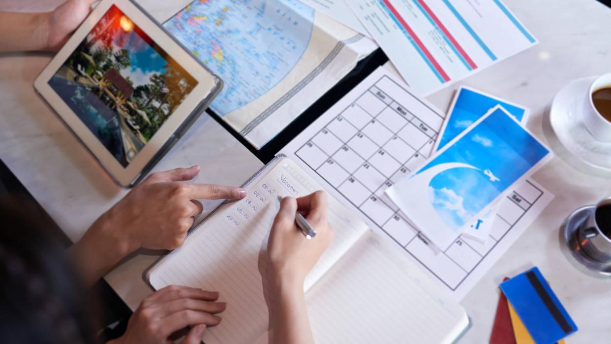 Close-up shot of unrecognizable couple taking necessary notes and planning vacation trip to Europe while sitting at table.