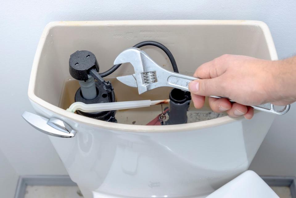A person holding a wrench near an open toilet tank to make a diy plumbing repair.