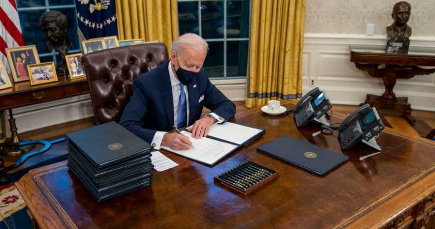 美國總統拜登在橢圓辦公室簽署文件。（圖／翻攝推特／Tom Newton Dunn）