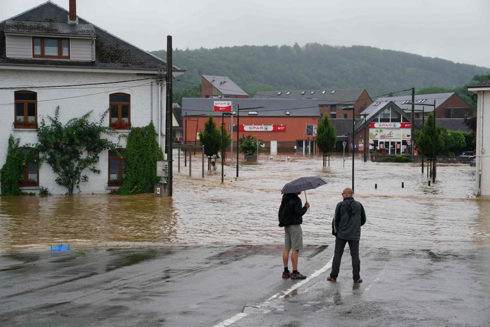 TOPSHOT - People stand by a flooded street in Rochefort on July 15 2021 as disaster plan has been declared in Belgium's provinces of Liege, Luxembourg and Namur after heavy rains and floods lashing western Europe have killed at least two people in the country. (Photo by ANTHONY DEHEZ / AFP)