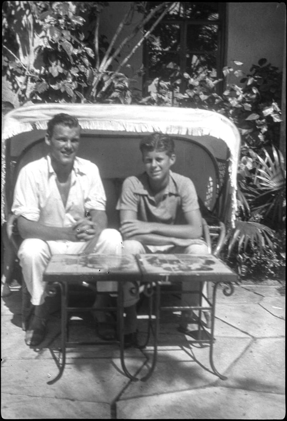 John F. Kennedy (right) and Kirk LeMoyne "Lem" Billings sit in a wicker chair outside the Kennedy family home in Palm Beach