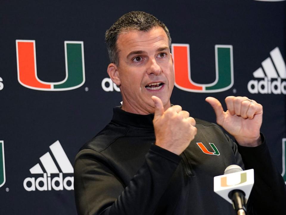 Mario Cristobal points with two thumbs during a press conference.