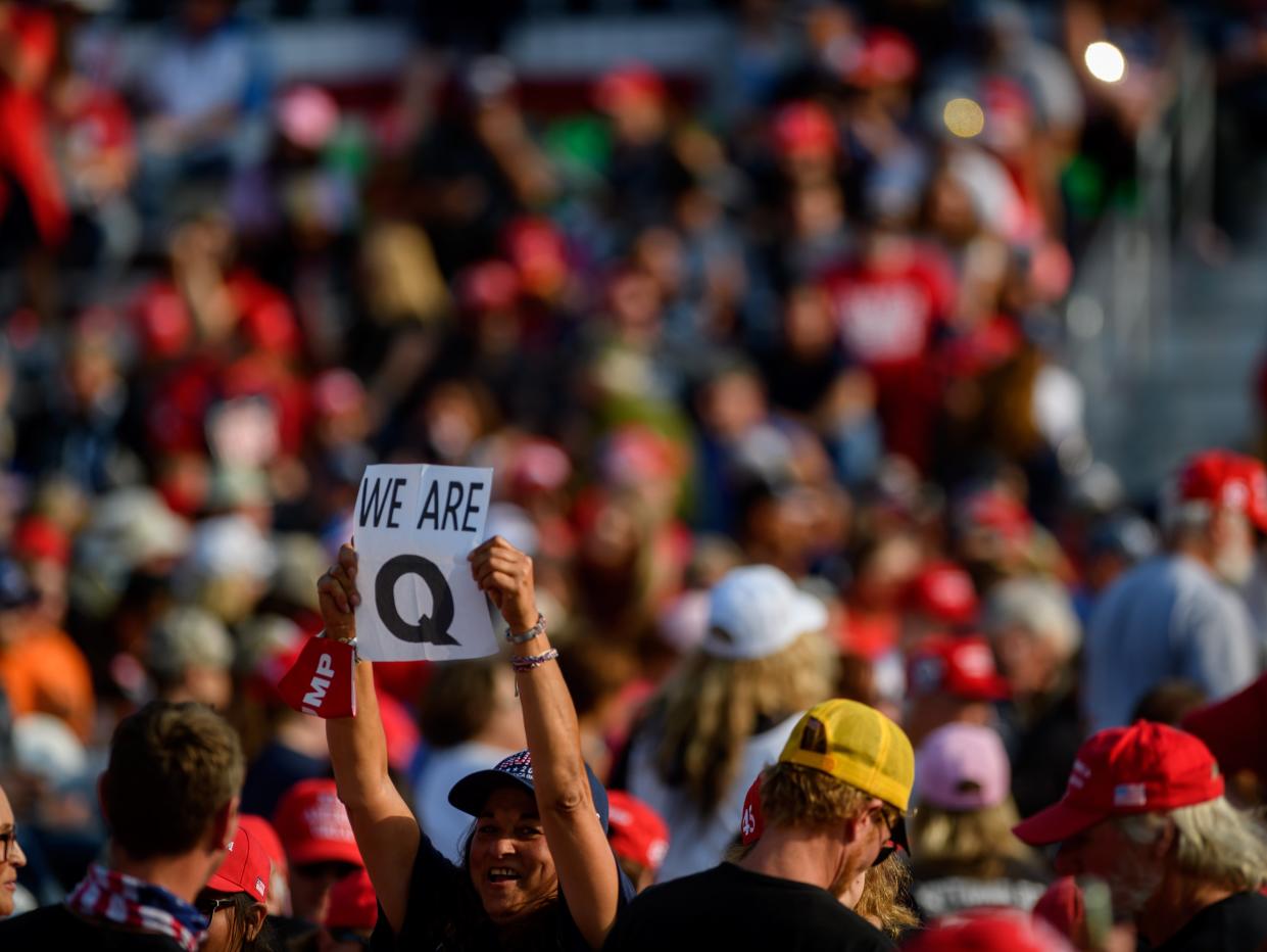A woman holds up a QAnon sign to the media as attendees wait for President Donald Trump to speak at a campaign rally ((Getty Images))
