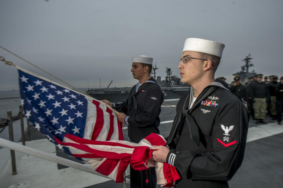 Logistics Specialist 3rd Class Logan Davidson, right, and Aviation Boatswain’s Mate (Handling) Airman Recruit Gabriel Gonzalez, conduct morning colors on the flight deck aboard the aircraft carrier <em>USS George H.W. Bush</em> (CVN 77) on Dec. 1. The flag was flown at half-mast to honor the 41st president, the ship’s namesake, who died on Friday. The ship is in port in Norfolk, Va., conducting routine training exercises to maintain carrier readiness. (Photo: Mass Communication Specialist 3rd Class Zachary P. Wickline/U.S. Navy via AP)