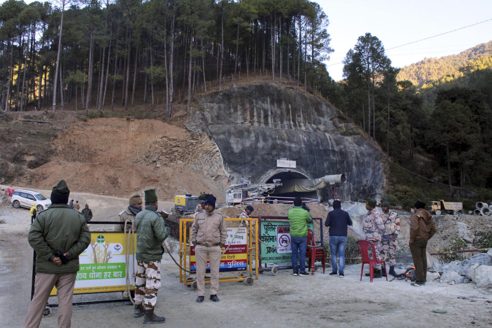 Security officers stand near the entrance to the site of an under-construction road tunnel that collapsed in mountainous Uttarakhand state, India, Friday, Nov. 17, 2023. Rescuers drilled deeper into the rubble of a collapsed road tunnel in northern India on Friday to fix wide pipes for 40 workers trapped underground for a sixth day to crawl to their freedom. (AP Photo)