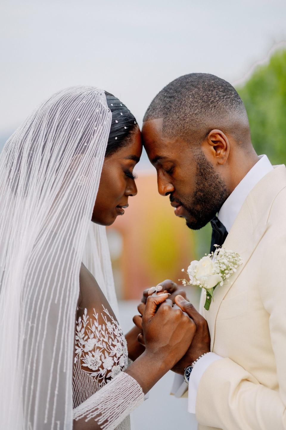 A bride and groom lean their foreheads together and hold hands.