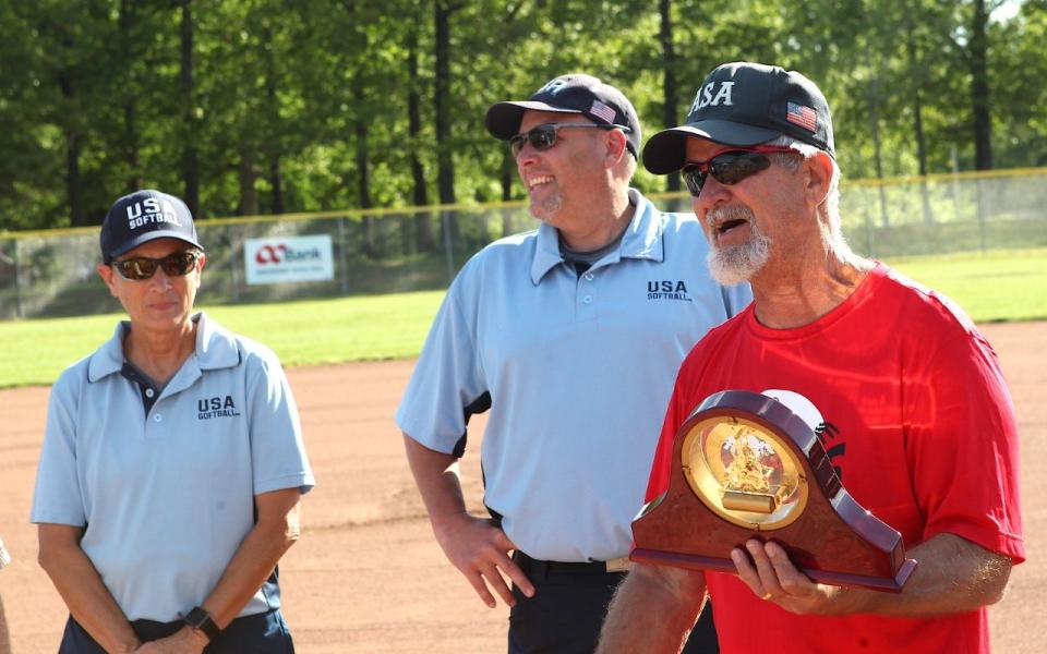 Fellow umpires Michelle Riester and Corey Hudson, BSA board president, look on as Ralph "Froggy" Poole shows off the clock he received from the Bedford Parks Department upon officially retiring after 39 years as a softball umpire.