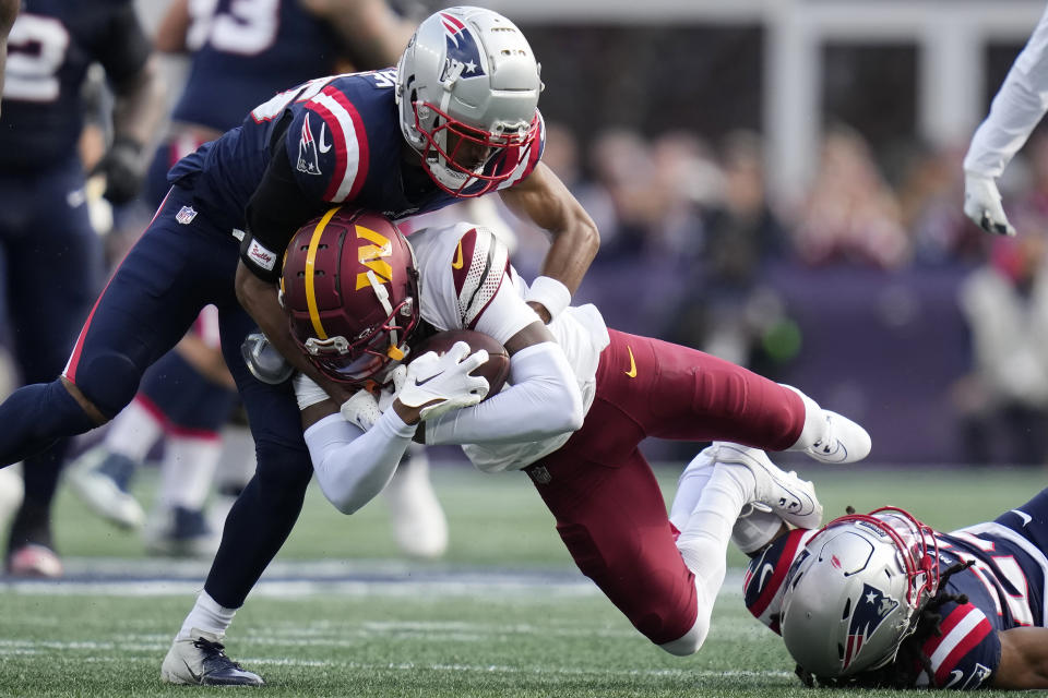 Washington Commanders wide receiver Dyami Brown, center, is brought down by New England Patriots cornerback Shaun Wade, left, and safety Kyle Dugger, right, in the first half of an NFL football game, Sunday, Nov. 5, 2023, in Foxborough, Mass. (AP Photo/Charles Krupa)