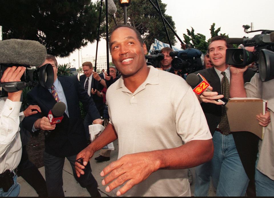 O.J. Simpson walking through a crowd of media personnel.