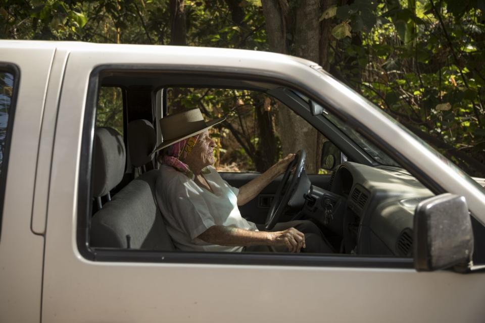 A woman in a head scarf and flat-brimmed hat sits at the wheel of a pickup.