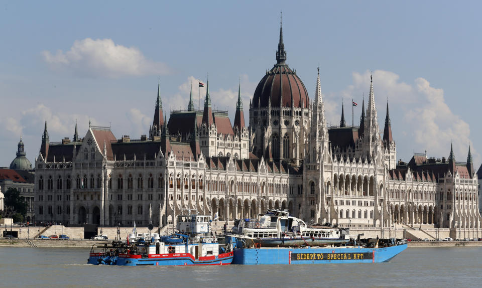 FILE - In this Tuesday, June 11, 2019, file photo, a barge carries the sightseeing boat, right, past the house of parliament on the Danube river after it was lifted from riverbed in Budapest, Hungary. Preparations are underway for commemorations to be held on the first anniversary of the May 29, 2019, mishap on the Danube River in which a sightseeing boat carrying mostly tourists from South Korea sank after a collision with a river cruise ship. Just seven of the 33 South Korean tourists aboard the Hableany (Mermaid) survived the nighttime collision. (AP Photo/Darko Bandic, File)