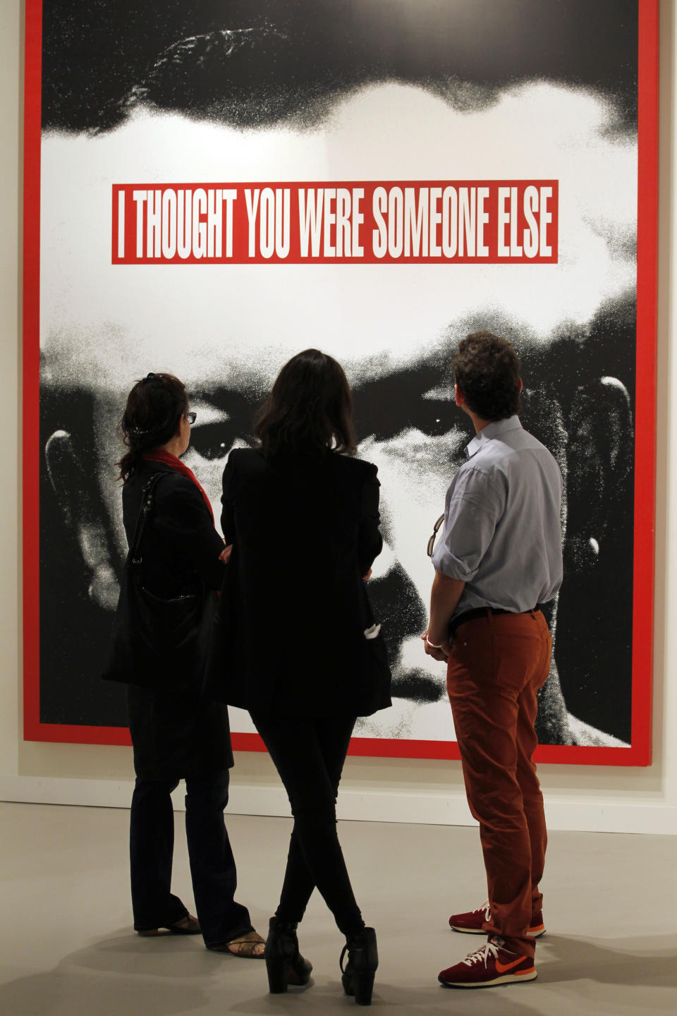 FILE - This Dec. 5, 2012 file photo shows a group of people look at a large work by Barbara Kruger "Untitled (I Thought You Were Someone Else)" on display as part of Art Basel Miami Beach in Miami Beach, Fla. The 2013 Art Basel Miami Beach takes place Dec. 5-8. (AP Photo/Wilfredo Lee, File)