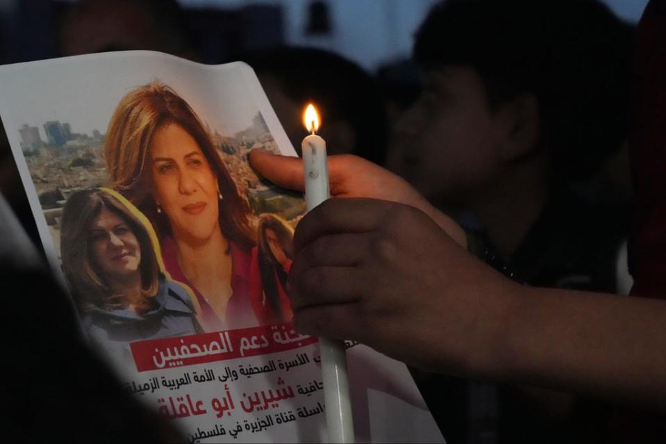 A Palestinian holds a light candle and a picture ofAl Jazeera journalist Shireen Abu Akleh, to condemn her killing, in front of the office of Al Jazeera network, in Gaza City (AP)