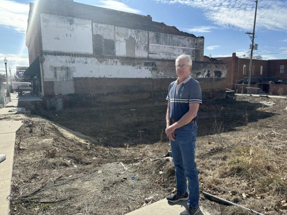 A man standing in an empty lot, where a building destoryed by fire once stood.