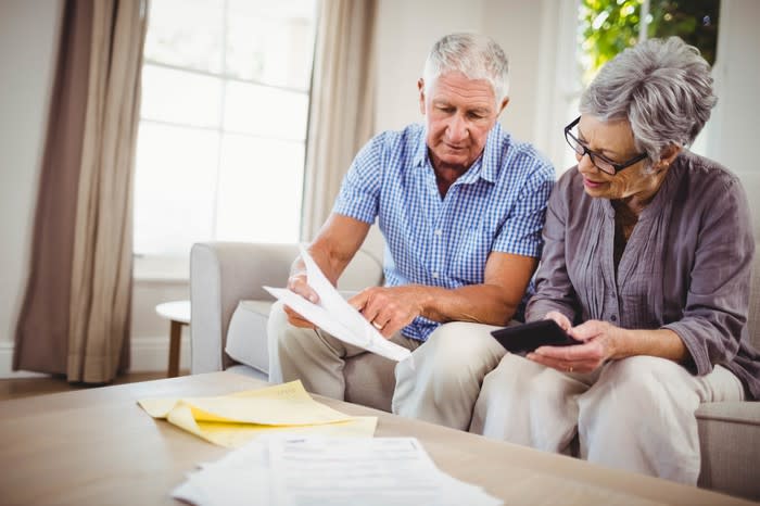 Older man and woman seated on a couch, looking at documents