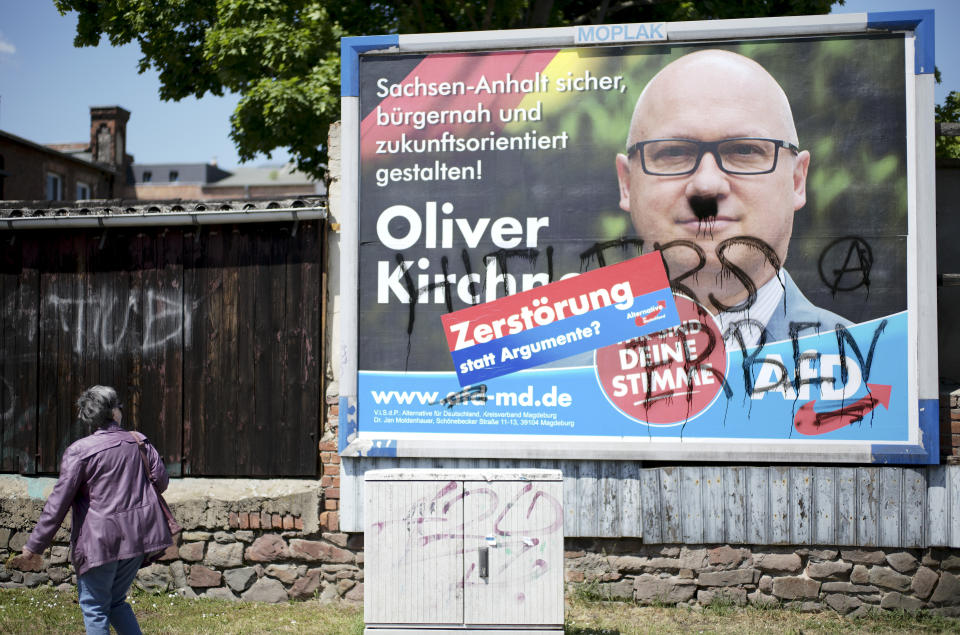 A vandalized election campaign poster for the far-right Alternative for Germany party showing the party's top candidate, Oliver Kirchner, stands on a road in Saxony-Anhalt's state capital of Magdeburg, Germany, Wednesday, June 2, 2021. The state vote on Sunday, June 6, 2021 is German politicians' last major test at the ballot box before the national election in September that will determine who succeeds Chancellor Angela Merkel. After a mustache and the words "Hitler's heirs" were sprayed on the poster, the party added a sticker reading: 'Destruction instead of arguments?' The AFD election campaign slogan reads: ' Make Saxony-Anhalt safe, close to the citizen and future-oriented'. (AP Photo/Markus Schreiber)