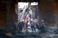 Police carry a body bag containing a body of a victim as workers remove debris in a gutted slipper factory in Valenzuela, Metro Manila in the Philippines May 14, 2015.A fire at a factory making rubber slippers killed 31 workers in the Philippine capital on Wednesday, and dozens were missing and feared dead, officials said. REUTERS/Erik De Castro