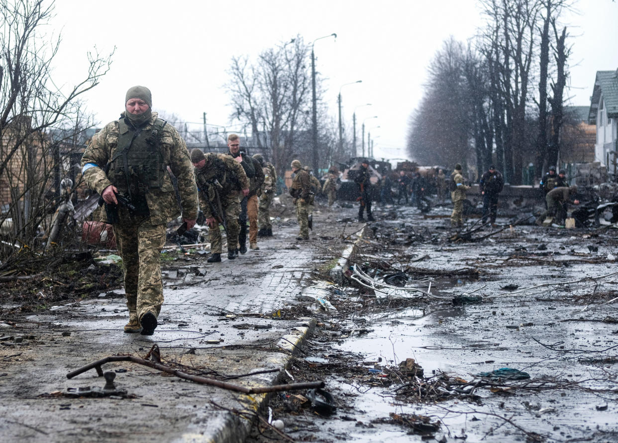 BUCHA, UKRAINE - 2022/04/03: Ukrainian soldiers inspect the wreckage of a destroyed Russian armored column on the road in Bucha, a suburb north of Kyiv. As Russian troops withdraw from areas north of Ukraine's capital city of Kyiv, Ukrainian forces and the media found evidence of significant numbers of civilian casualties. The Ukrainian authorities are calling the killing of civilians in Bucha and other areas a war crime. (Photo by Matthew Hatcher/SOPA Images/LightRocket via Getty Images)