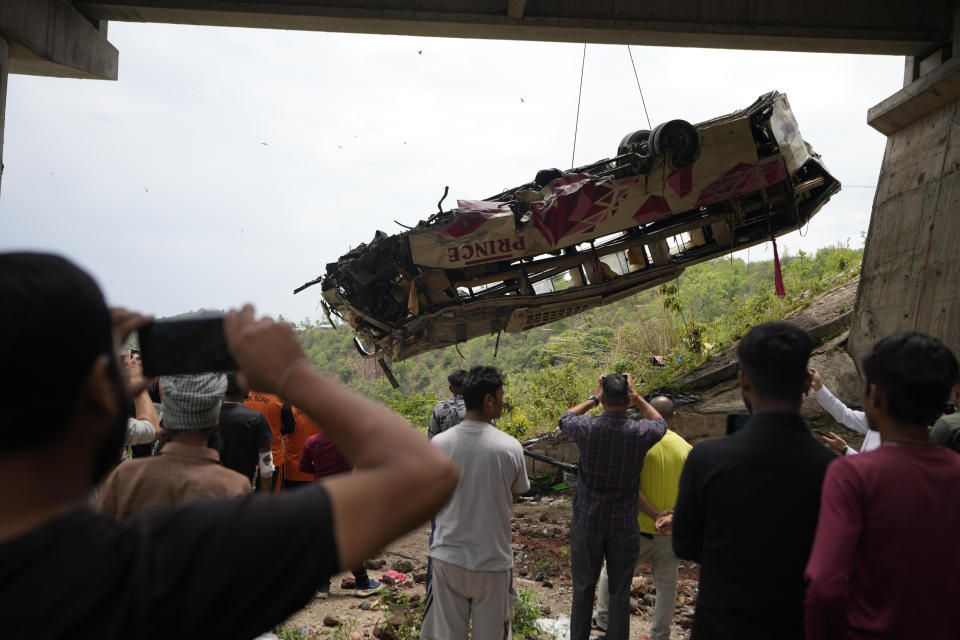 People watch rescuers use a crane after a bus carrying Hindu pilgrims to a shrine skid off a highway bridge into a Himalayan gorge near Jammu, India, Tuesday, May 30, 2023. (AP Photo/Channi Anand)