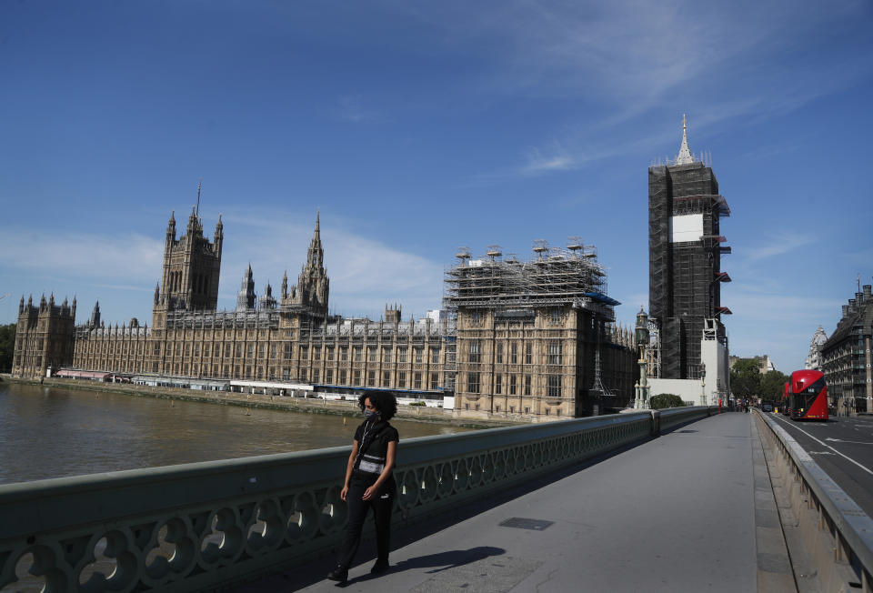 A pedestrian walks over Westminster Bridge alongside Parliament in London, Tuesday, June 2, 2020. The British government has decided to scrap a remote-voting system used during the coronavirus pandemic, and has summoned lawmakers back to parliament on Tuesday, but many aren't happy with the arrangements. (AP Photo/Frank Augstein)