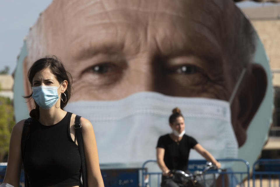 An Israeli woman walks past a banner encouraging people to wear face masks in Tel Aviv, Israel, Thursday, Sept. 24, 2020. Israeli Prime Minister Benjamin Netanyahu on Wednesday announced plans for a strict, two-week nationwide lockdown in a bid to slow a raging coronavirus outbreak. (AP Photo/Sebastian Scheiner)