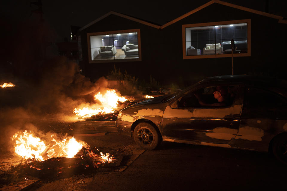 A man drives past a burning barricade that was set up to protest the detention of people by the police at the Puerta 8 low-income neighborhood of Buenos Aires, Argentina, Wednesday, Feb. 2, 2022. Authorities say that those detained were involved in the sale of adulterated cocaine that has killed more than a dozen people and sent at least 50 others to the hospital. (AP Photo/Rodrigo Abd)