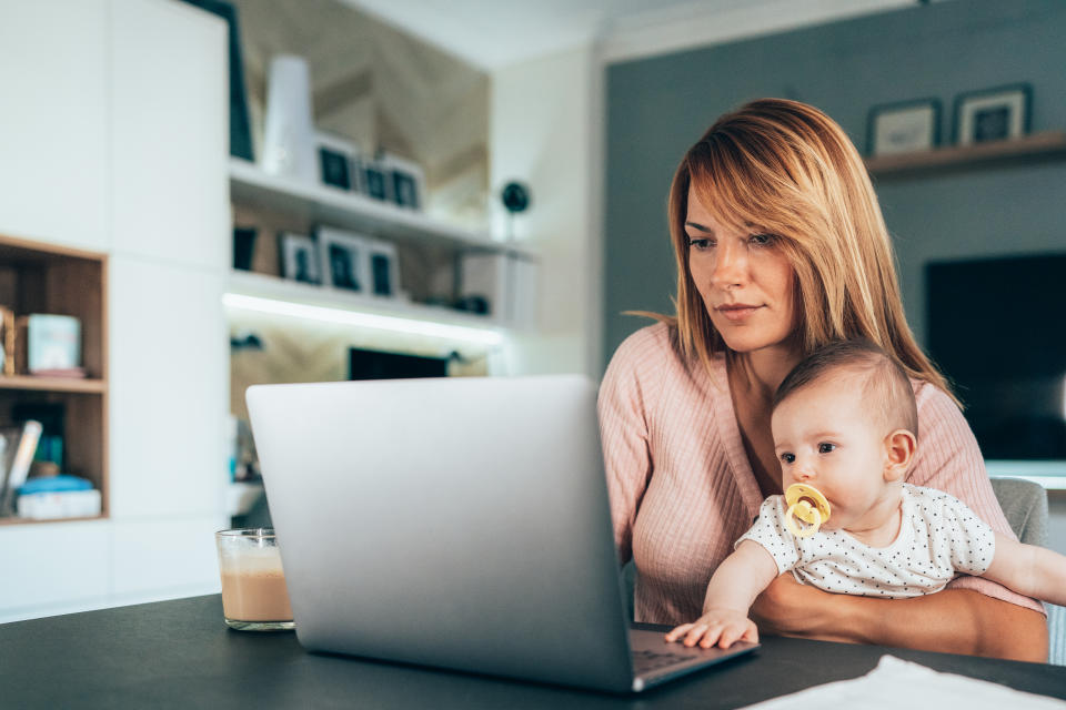 Shot of a young woman working at home, using laptop while holding her cute baby Maternity pay
