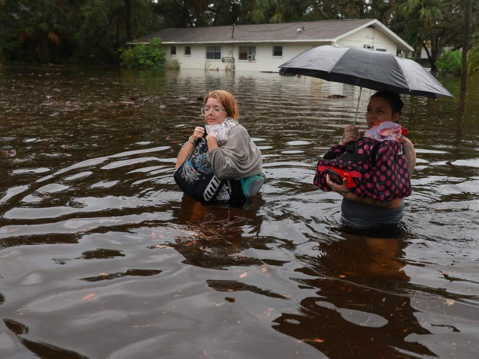 Two women wade through waist-deep water carrying items from their homes.