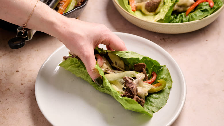 hand picking up steak lettuce wrap on plate