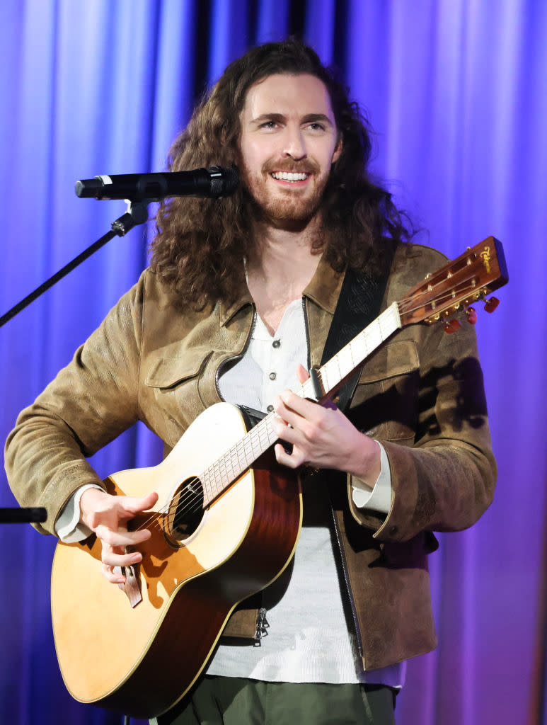 Hozier with long curly hair holding a guitar as he performs onstage